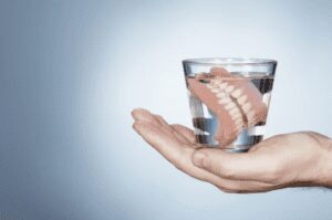 open hand holding a glass filled with water and soaking dentures restorative dentistry dentist in Ardmore Pennsylvania